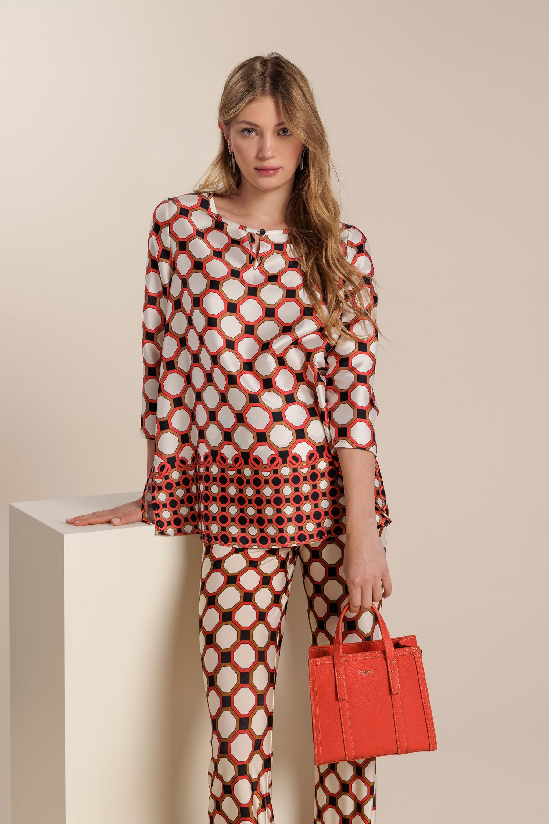 Mujer portando un conjunto de blusa y pantalón con estampado geométrico y un bolso de color rojo